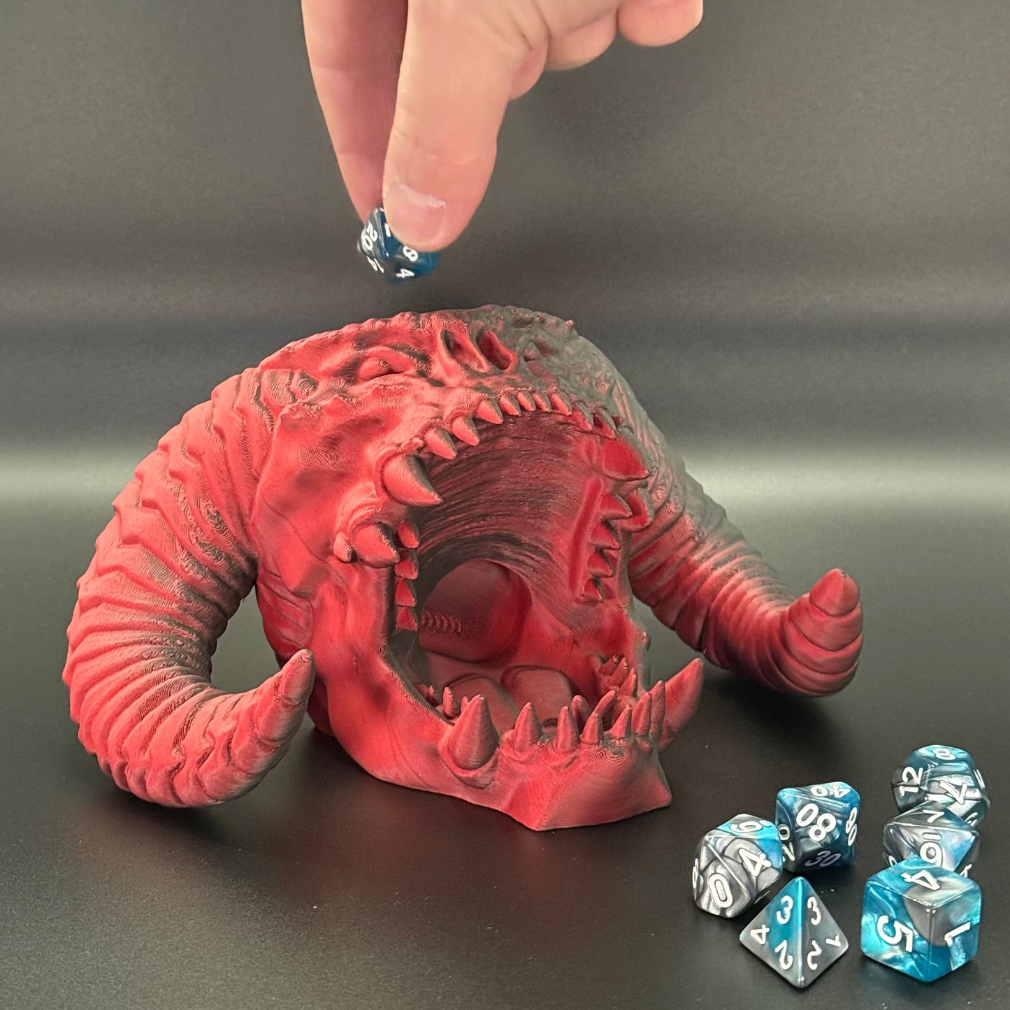 Red fantasy creature figurine with blue and silver dice on a gray background
